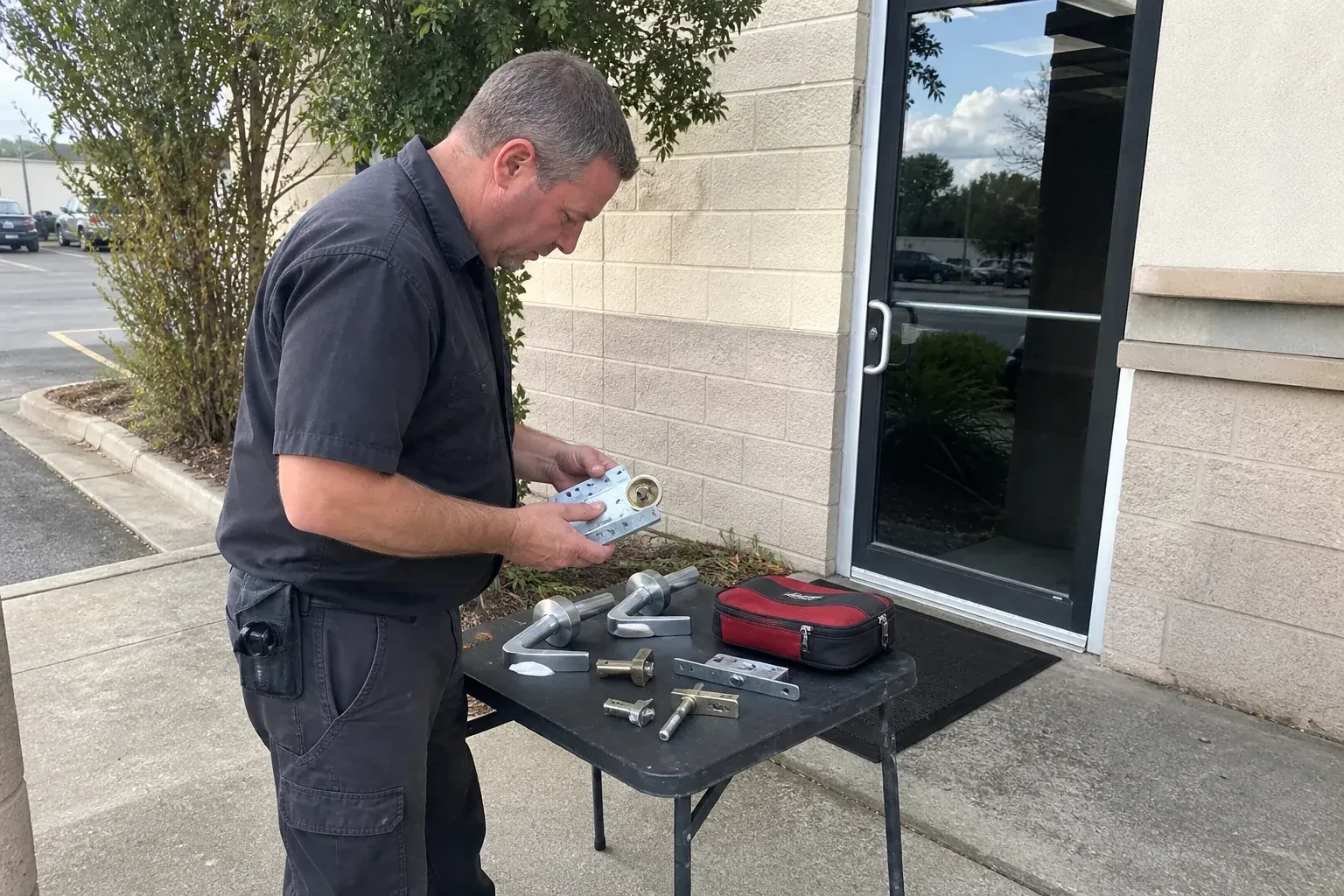 Technician examining detached commercial lock hardware on a table outside a shop entrance. — Business Lockout Service, Brampton